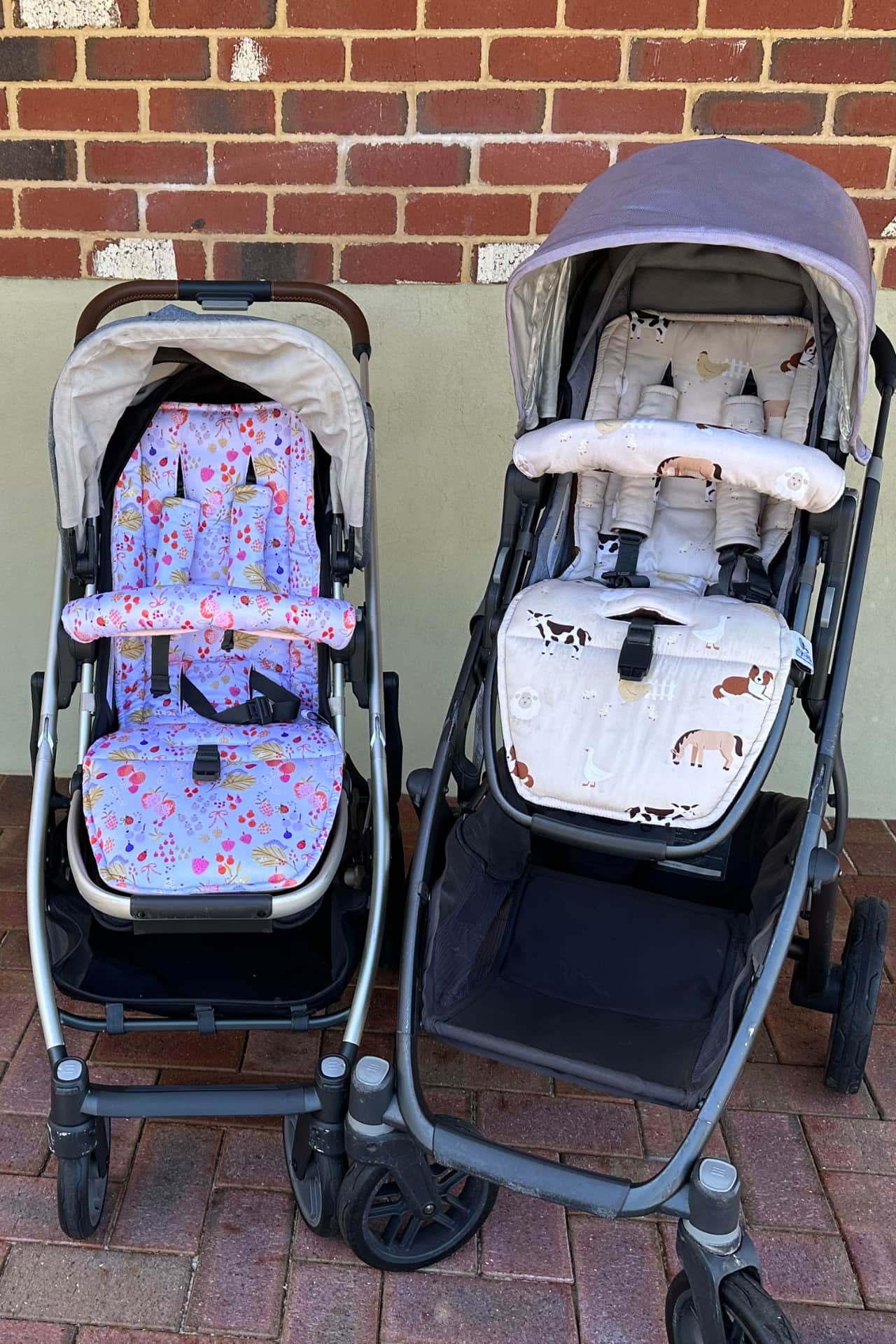 Two strollers with patterned seats on a brick pavement.